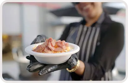Gloved chef holding a bowl of food topped with sliced meat